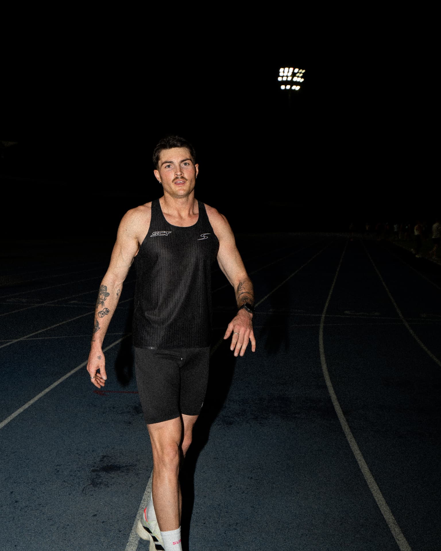 Runner walking down the track lane under stadium lights