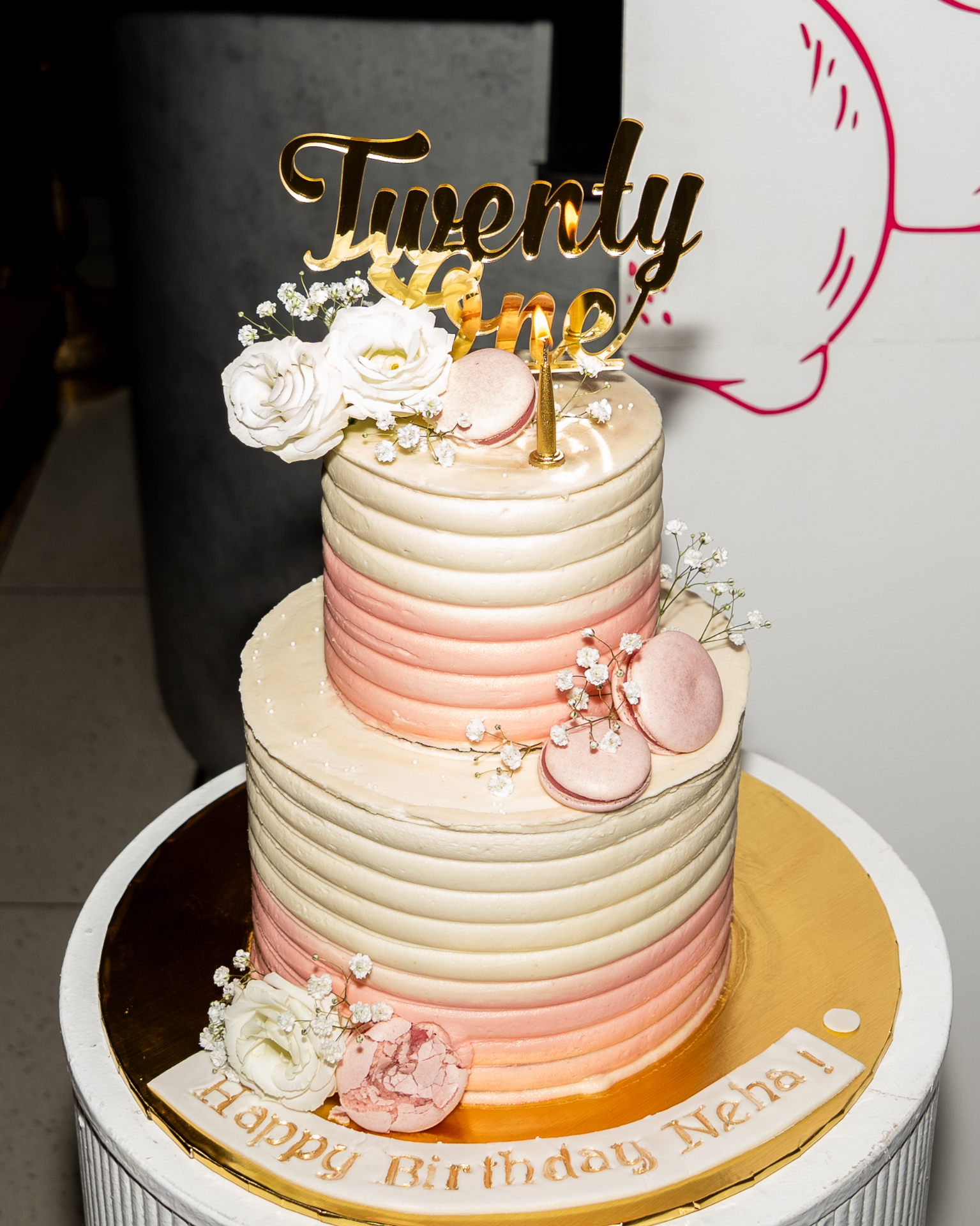 Two-tier pink and white birthday cake with macarons
